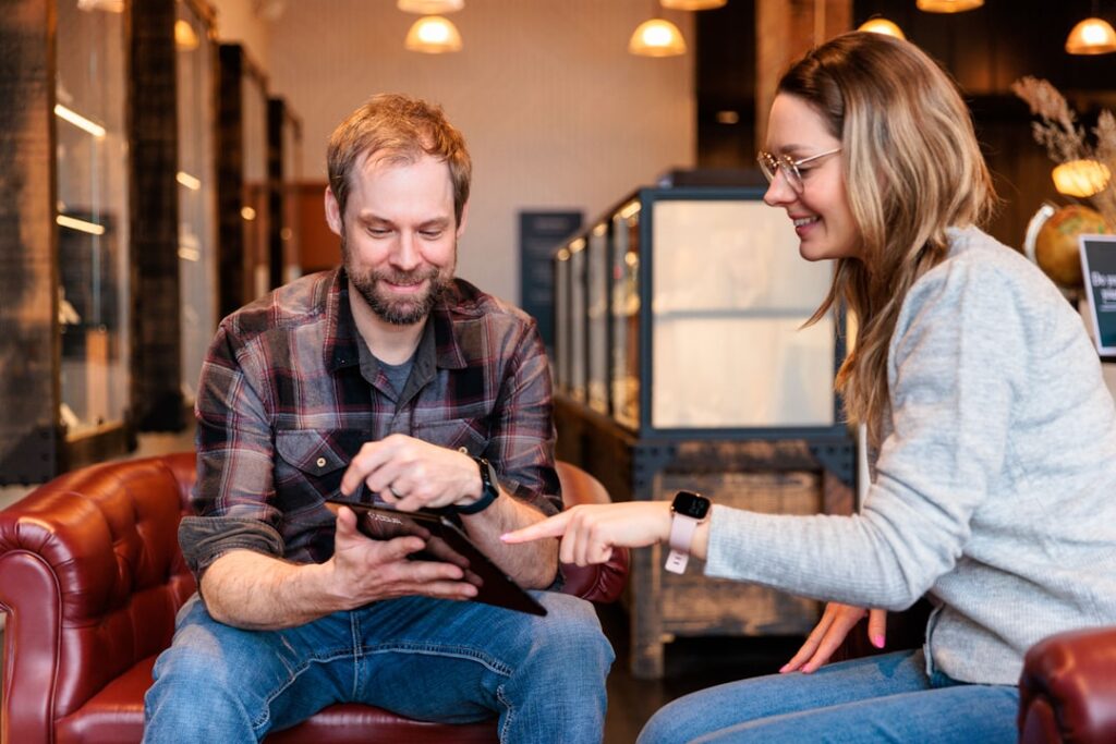 Professional real estate agent stands with a smiling couple in a modern home, pointing to information on a digital tablet.