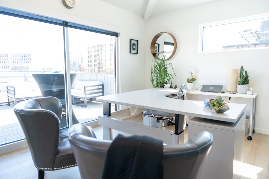 Professional, diverse couple sits at a bright, modern wooden table, attentively reviewing and signing legal documents for ...