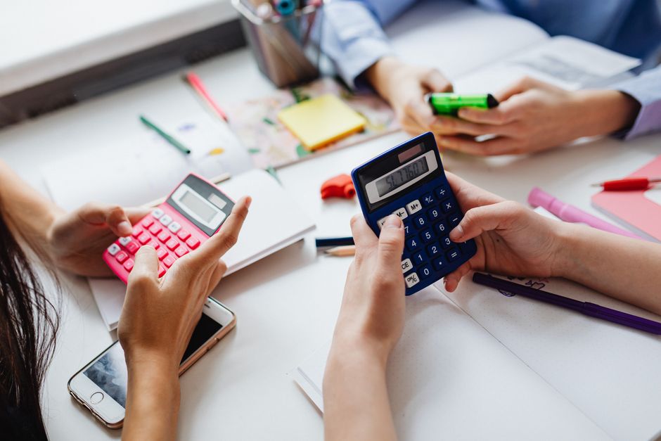 Bright, professional flatlay of a calculator, house keys, and a notepad on a clean wooden desk, symbolizing the financial ...