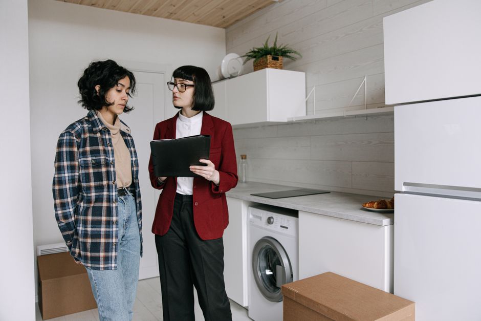 Two professional women, a realtor and a client, discussing documents at a sunlit kitchen island in a modern home, representing a collaborative and expert real estate partnership.